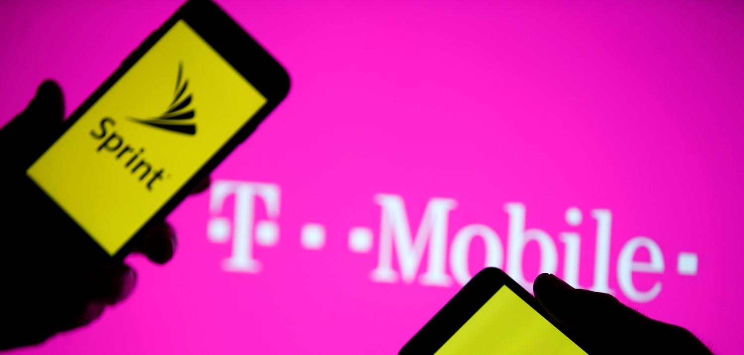 A smartphones with Sprint logo are seen in front of a screen projection of T-mobile logo.