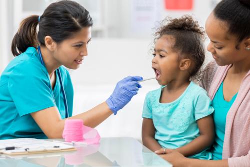 medical professional examines a young female patient's throat. The doctor is using a tongue depressor.