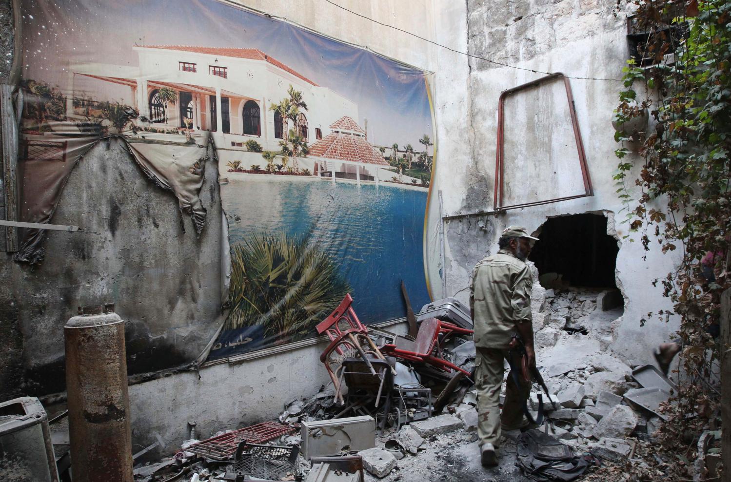 A Free Syrian Army fighter walks past a torn poster amid the rubble in the old city of Aleppo August 27, 2013. REUTERS/Muzaffar Salman (SYRIA - Tags: POLITICS CONFLICT) - GM1E98S046P01