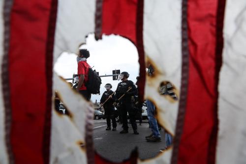 Police in riot gear and a protester stand near a burned U.S. flag after the not guilty verdict in the murder trial of Jason Stockley, a former St. Louis police officer charged with the 2011 shooting of Anthony Lamar Smith, in St. Louis, Missouri, U.S. September 17, 2017. Picture taken September 17, 2017.  REUTERS/Lawrence Bryant - RC17ECB258C0