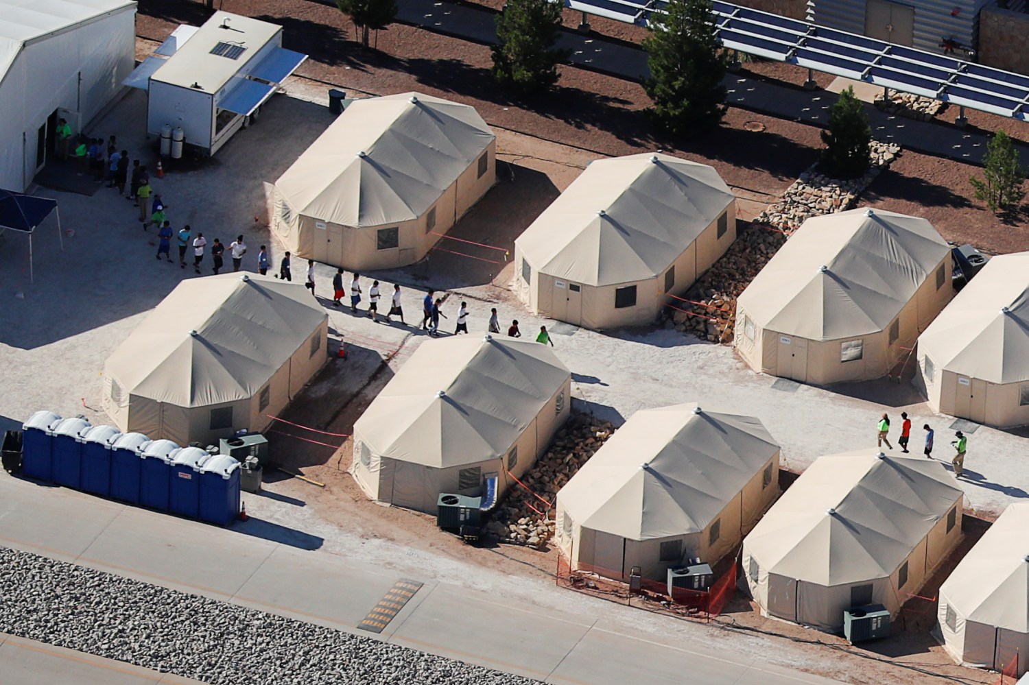 Immigrant children, many of whom have been separated from their parents under a new "zero tolerance" policy by the Trump administration, are shown walking in single file between tents in their compound next to the Mexican border in Tornillo, Texas, U.S. June 18, 2018.        REUTERS/Mike Blake - RC1A59D1E150