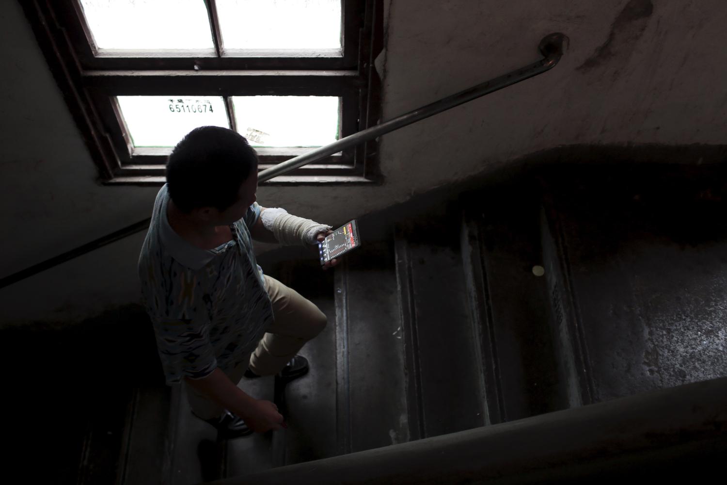 Gao Haibao, looks at stock information on his mobile phone as he climbs the stairs to his apartment.