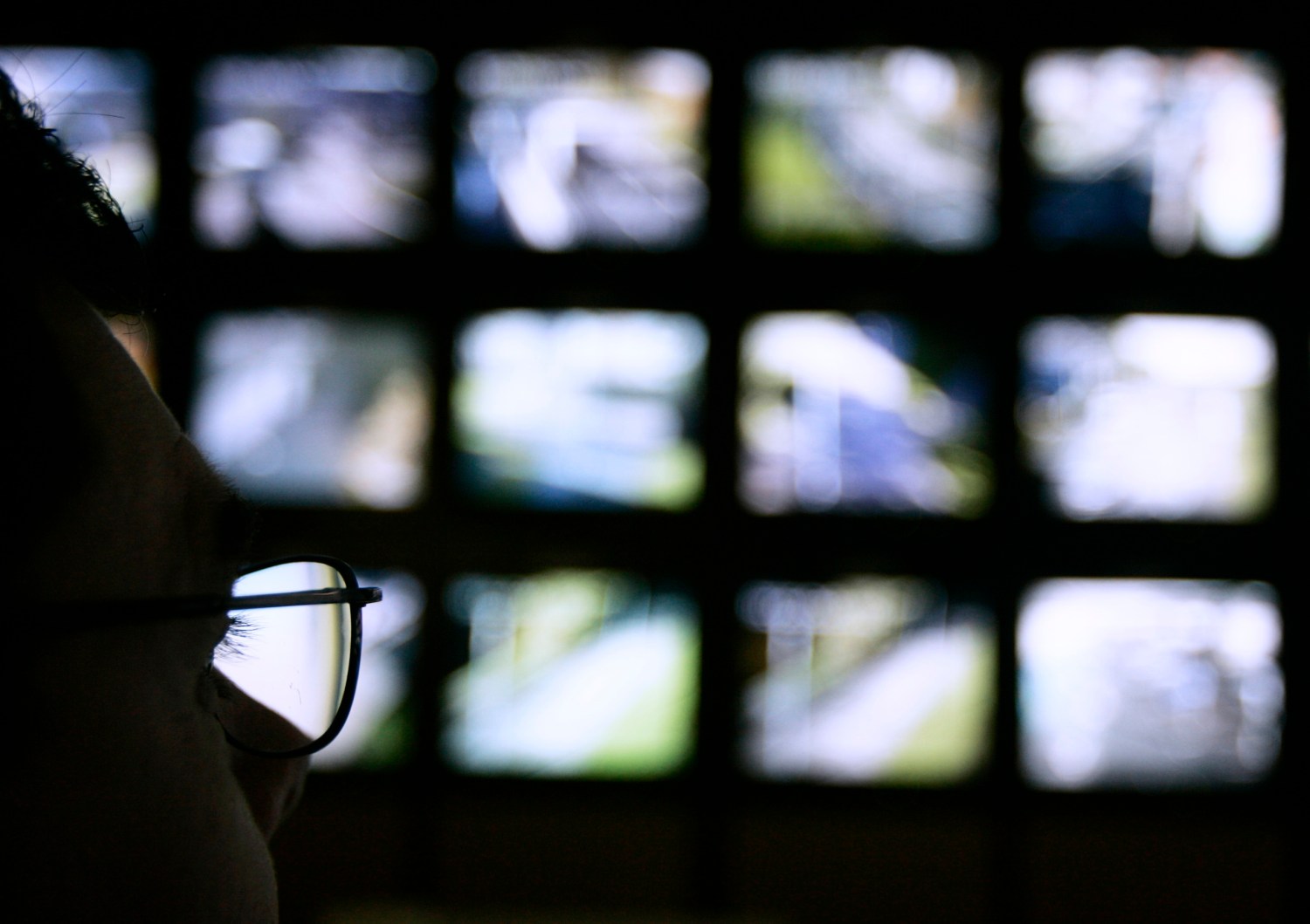 A surveillance monitoring expert watches a bank of screens showing images from CCTV cameras