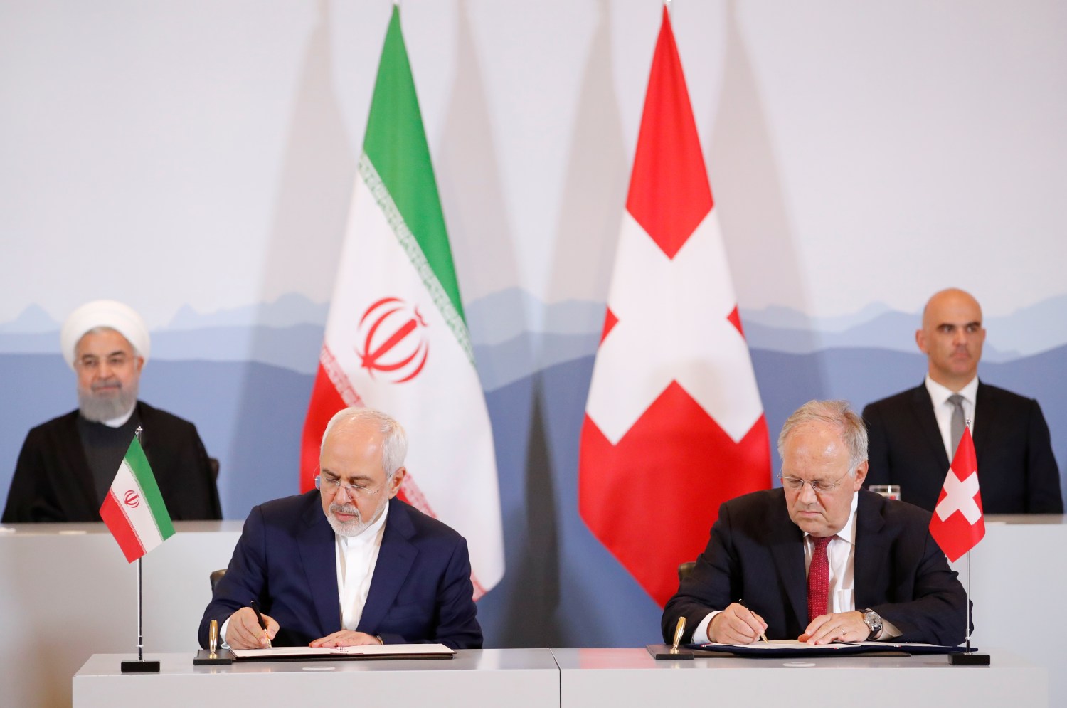 Swiss President Alain Berset and Iranian President Hassan Rouhani look on as Johann N. Schneider-Ammann, Head of the Federal Department of Economic Affairs, Education and research and Iran's Foreign Minister Mohammad Javad Zarif sign documents during an official visit in Bern, Switzerland, July 3, 2018. REUTERS/Denis Balibouse