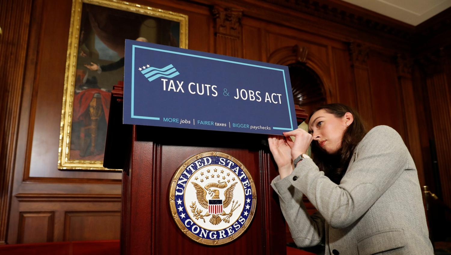 An aide adjusts a sign prior to a news conference announcing the passage of the "Tax Cuts and Jobs Act."