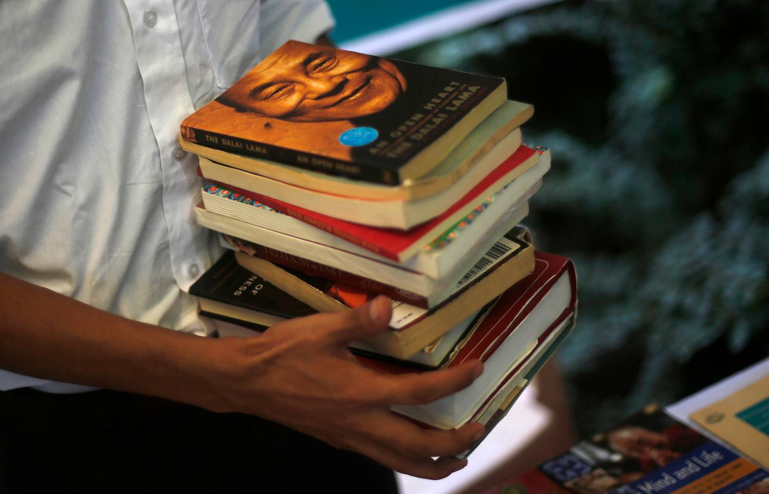 A Tibetan exile carries a stack of books for display with a portrait of Tibetan spiritual leader Dalai Lama at the top during celebrations of his 78th birthday at Majnu Ka Tila, a Tibetan refugee camp in New Delhi July 6, 2013. REUTERS/Adnan Abidi (INDIA - Tags: RELIGION SOCIETY TPX IMAGES OF THE DAY) - GM1E9761LDE01