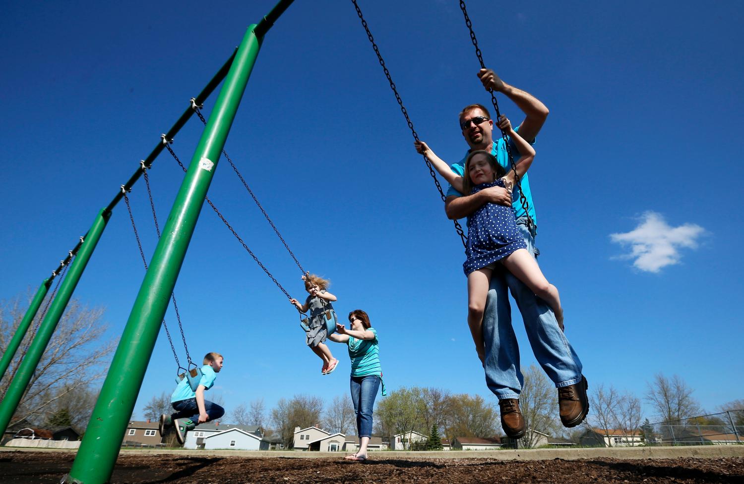 Joe Smith rides on a swing with his daughter Rowan as his wife Andrea plays with her children Norah and Chase  at a playground in Winthrop Harbor, Illinois, May 9, 2014. Three of their children have been diagnosed with atypical Hemolytic Uremic Syndrome, and one is a carrier which was diagnosed using genome sequencing. Once strictly the domain of research labs, gene-sequencing tests increasingly are being used to help understand the genetic causes of rare disease, putting insurance companies in the position of deciding whether to pay the $5,000 to $17,000 for the tests. Genetics experts say that sequencing more than doubles the chances that families get a diagnosis, and saves spending on multiple tests of single genes. Even if no treatment is found, the tests can also end hugely expensive medical odysseys as parents frantically search for the cause of their child's furtive illness. Picture taken May 9, 2014. To match Insight HEALTH-SEQUENCING/    REUTERS/Jim Young (UNITED STATES - Tags: SCIENCE TECHNOLOGY HEALTH SOCIETY BUSINESS) - GM1EA6J1MA301