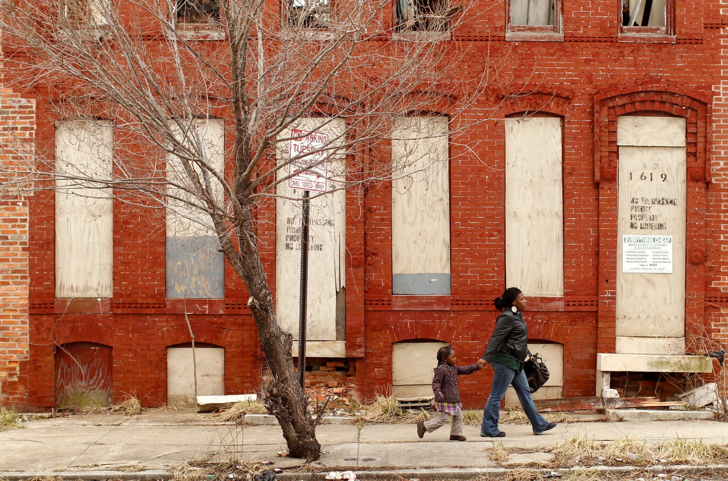 A woman and child walk past a dilapidated building in a run-down neighborhood of Baltimore, Maryland March 9, 2011. REUTERS/Kevin Lamarque (UNITED STATES - Tags: SOCIETY) - GM1E73A0I1C01