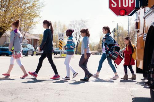 Multi-Ethnic Group of elementary school kids getting out a yellow school bus at school's out. Boys and girls age 6-11. They walk on behind another. They cross the street and the Stop sign of the yello school bus is open.  This was taken in Canada.