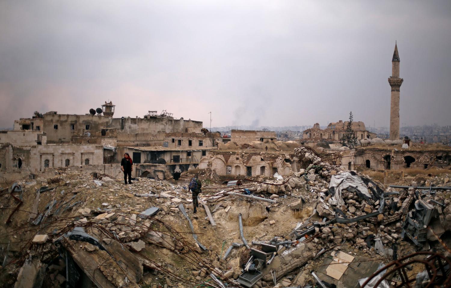 A member of forces loyal to Syria's President Bashar al-Assad stands with a civilian on the rubble of the Carlton Hotel, in the government controlled area of Aleppo, Syria December 17, 2016. REUTERS/Omar Sanadiki - RC181701B570