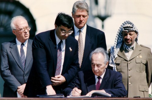 Israeli Foreign Minister Shimon Peres (sitting 2nd R) signs the Israeli-PLO peace accord as then PLO Chairman Yasser Arafat (R), then Israeli Prime Minister Yitzhak Rabin (L) and then U.S. President Bill Clinton (back C) stand behind him during a ceremony, at the White House in Washington September 13, 1993. REUTERS/Gary Hershorn (UNITED STATES - Tags: POLITICS) - GM1E99D1UC401