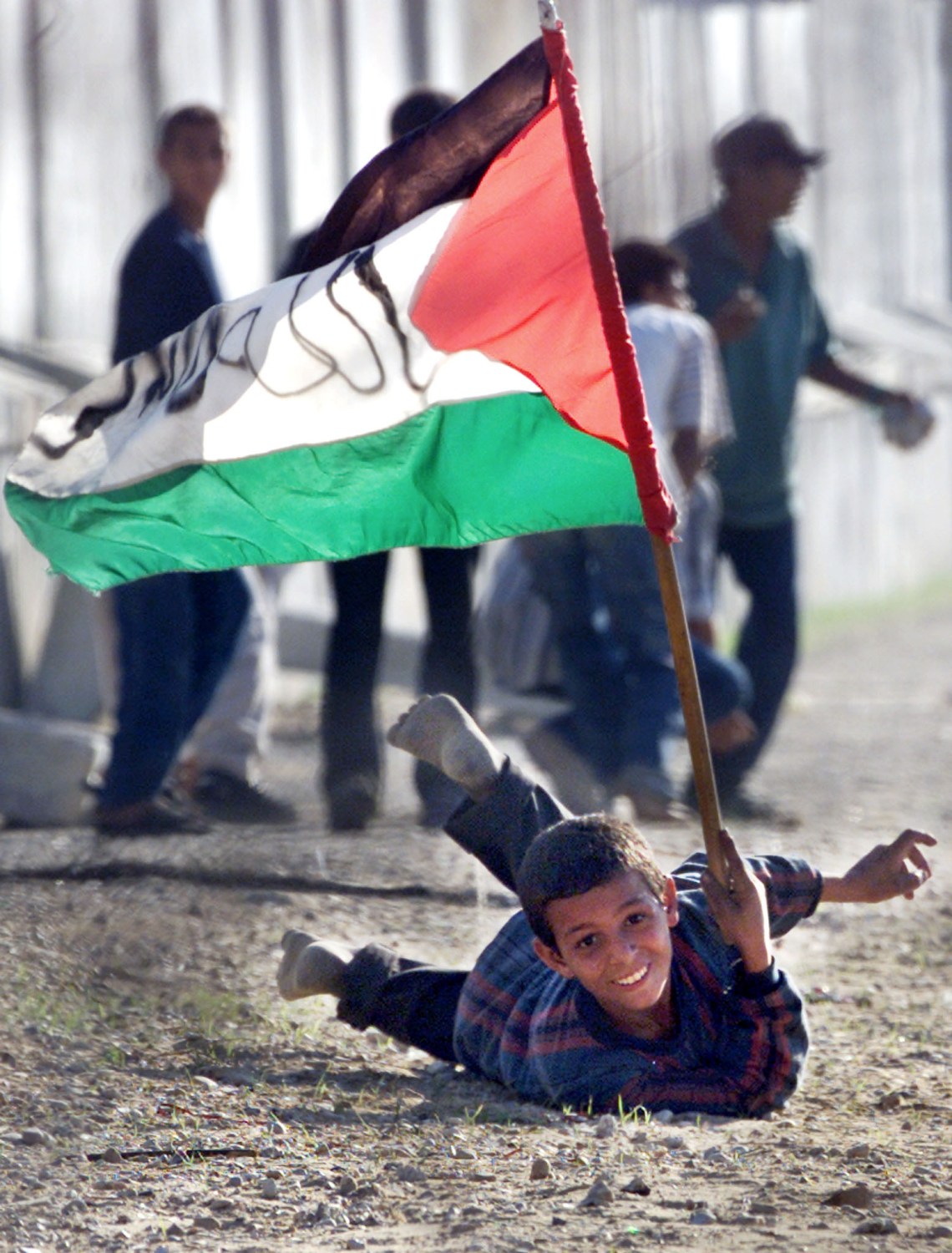 A Palestinian boy holding a Palestinian flag takes shelter from Israeli gunfire during clashes with Israeli soldiers at Gush Kitaf Jewish settlement near Khan-Younes south of the Gaza Strip November 7, 2000.JFL/FMS - RP2DRHYJWXAA