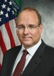Marshall Billingslea, Assistant Secretary for Terrorist Financing, US Department of treasury posing in fornt of the American flag with a gray backdrop