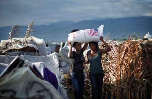Two women carry a bag of rice from USAID as part of food distributed by various relief agencies in Cite Soleil, Port-au-Prince February 18, 2010. France will provide 270 million euros (US$366.8 million) over two years to Haiti to help the Caribbean nation's economy recover from a devastating January 12 earthquake, France's President Nicolas Sarkozy said on Wednesday. REUTERS/Carlos Barria (HAITI - Tags: DISASTER ENVIRONMENT FOOD POLITICS SOCIETY) - GM1E62J06H202