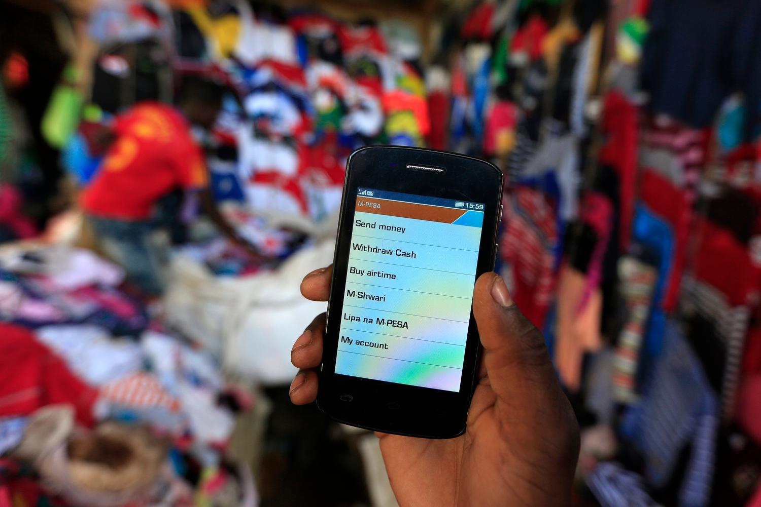 A man holds up his mobile phone showing a M-Pesa mobile money transaction page for the photographer at an open air market in Kibera in Kenya's capital Nairobi December 31, 2014. Safaricom, Kenya's biggest telecoms firm, is a model of how technology can be used to financially include millions of people with mobile telephones but without access to traditional infrastructure such as the banks that are available to the wealthy or those living in cities. Safaricom in 2007 pioneered its M-Pesa mobile money transfer technology, now used across Africa, Asia and Europe. It proved that money can be made from people who earn a few dollars a day.  REUTERS/Noor Khamis (KENYA - Tags: BUSINESS SOCIETY SCIENCE TECHNOLOGY TELECOMS) - GM1EACV1IZY01