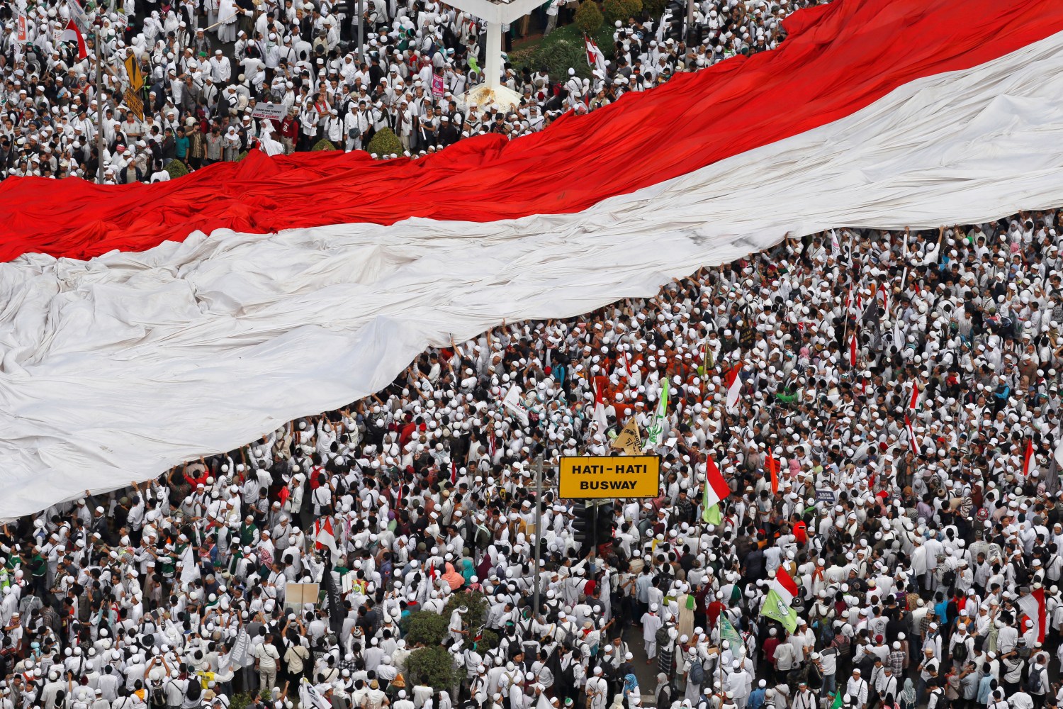 Members of hardline Muslim groups hold a big national flag as they attend a protest against Jakarta's incumbent governor Basuki Tjahaja Purnama