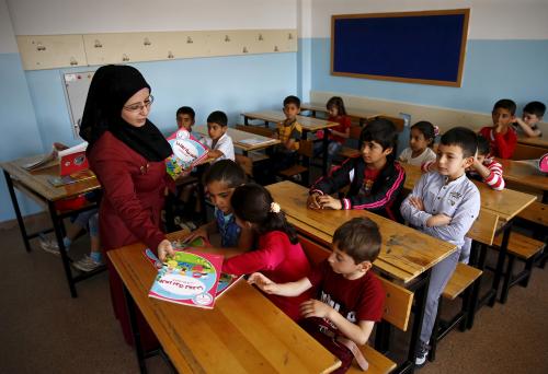 A Syrian refugee teacher distributes books to her refugee students in their classroom at Fatih Sultan Mehmet School in Karapurcek district of Ankara, Turkey, September 28, 2015. Out of 640,000 Syrian children in Turkey, 400,000 are not at school, a Turkish official told Reuters on Friday, warning that those who miss out are likely to be exploited by "gangs and criminals". Educating the children among more than 2.2 million Syrian refugees in Turkey - most of whom live outside purpose-built camps - is seen as a critical part of the humanitarian response to the four-and-a-half-year-old conflict. Picture taken September 28, 2015. REUTERS/Umit Bektas  - GF10000230197