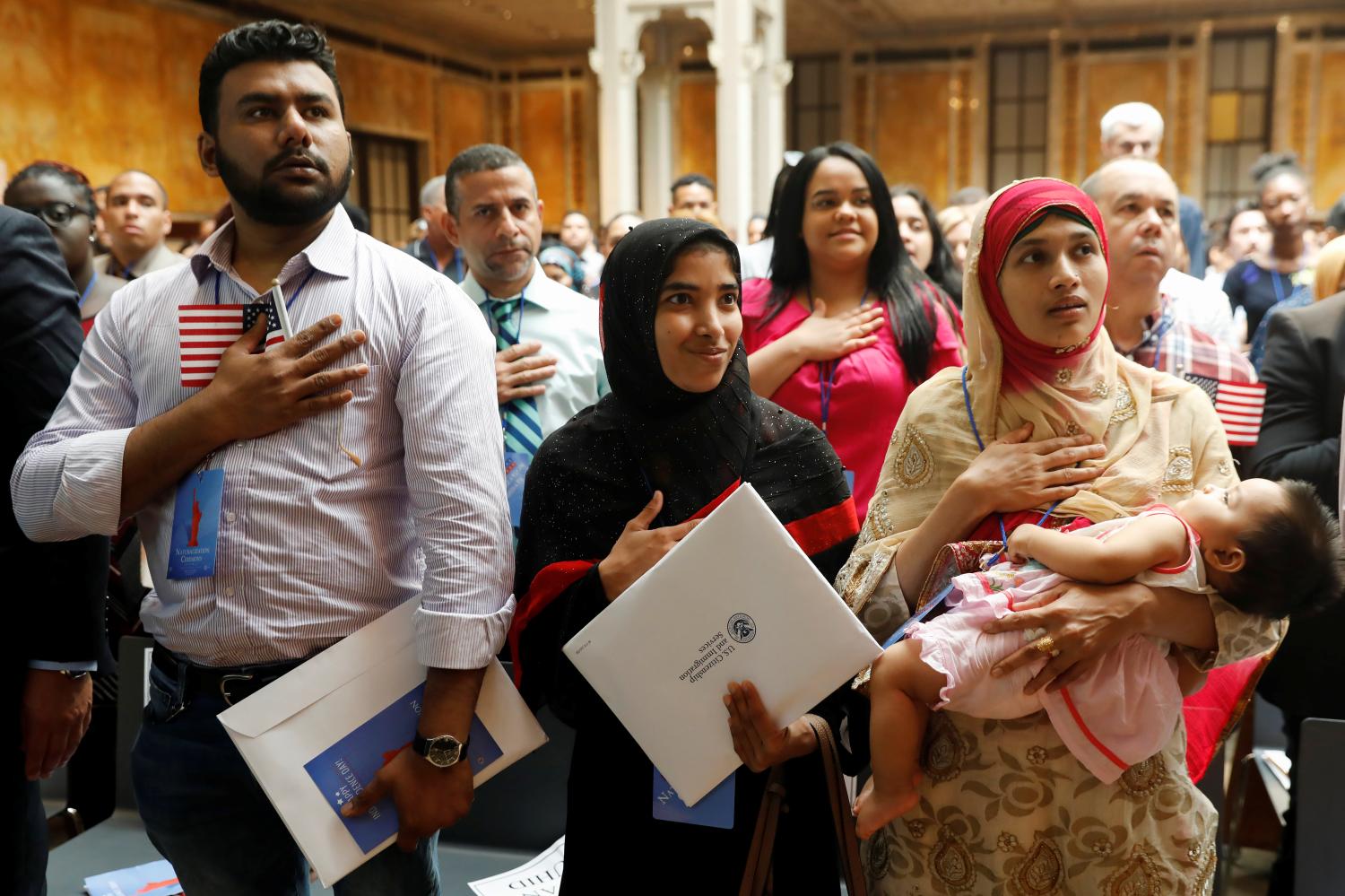 New citizens stand during the National Anthem at a U.S. Citizenship and Immigration Services (USCIS) naturalization ceremony at the New York Public Library in Manhattan, New York, U.S., July 3, 2018.  REUTERS/Shannon Stapleton - RC1DCBADC590