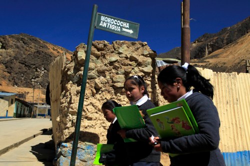 School girls walk in front of a sign at the ramshackle town of Morococha in the Andean city of Junin, June 18, 2012. High in the Andes mountain range, a Chinese mining company is now in the housing construction and demolition business as it works to relocate a Peruvian town that sits in the way of its $2.2 billion Toromocho copper mine. By late July, state-owned miner Chinalco says it will finish building a new city of paved roads and multi-story homes for 5,000 people currently living on the side of a giant red mountain of copper 15,000 feet (4,500 meters) above sea level. Picture taken June 18, 2012. To match Feature PERU-MINING/CHINALCO  REUTERS/Pilar Olivares (PERU - Tags: POLITICS ENVIRONMENT) - GM1E8711UBF01