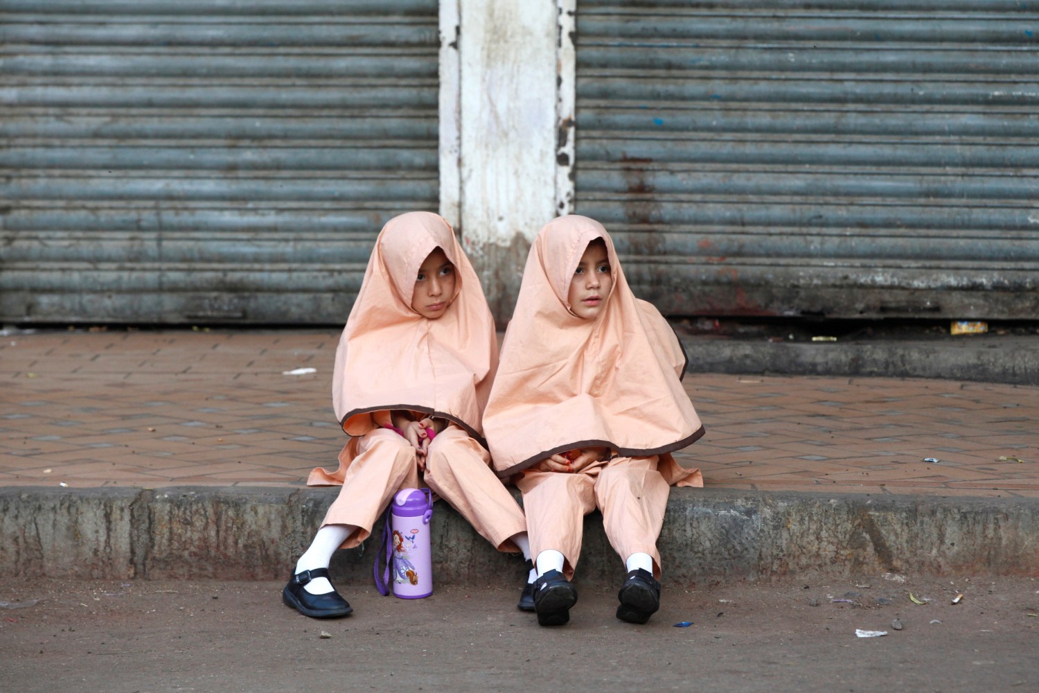 Girls in uniform sit along a sidewalk while waiting for school van in Karachi, Pakistan November 8, 2017. REUTERS/Akhtar Soomro - RC124BAB2DC0