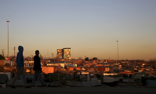 Unused cooling towers are seen overlooking an informal settlement as locals walk before sunset in Soweto, South Africa August 5, 2015. REUTERS/Siphiwe Sibeko - GF20000014477