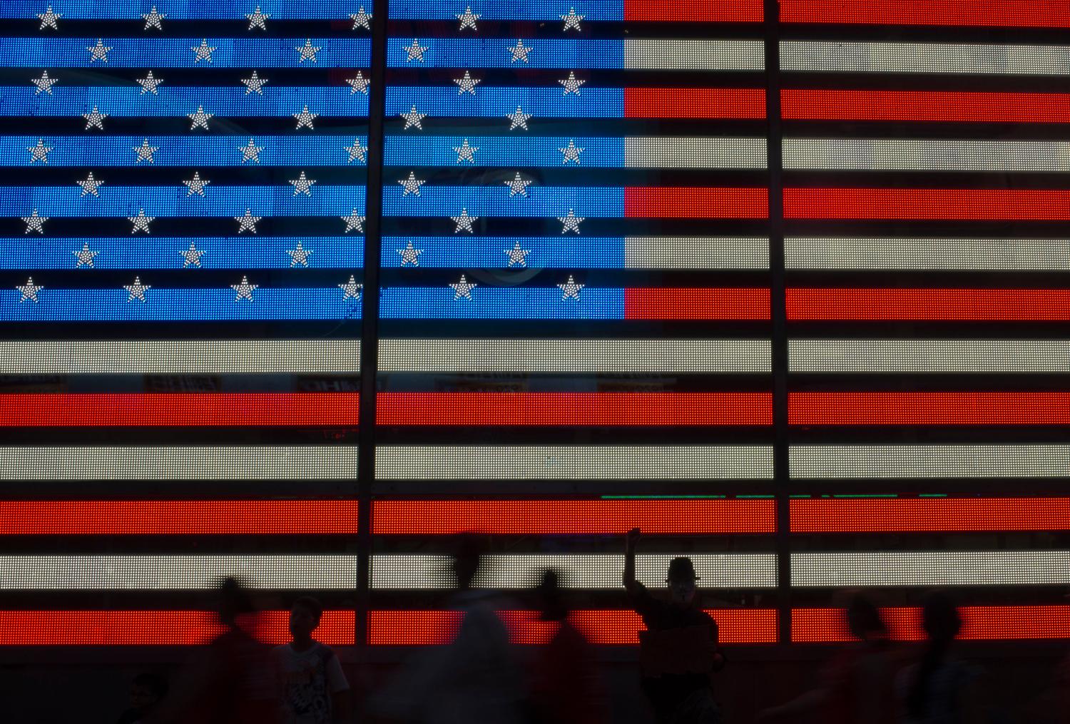 An Occupy Wall Street movement activist raises his fist while protesting in front of a digital flag of the United States in Manhattan's Time Square in New York on July 17, 2012.  REUTERS/Adrees Latif  (UNITED STATES - Tags: CIVIL UNREST SOCIETY) - GM1E87I0W6M01