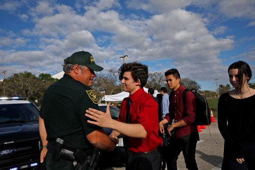 Alfonso Calderon (C), a student who was at Marjory Stoneman Douglas High School during the mass shooting, greets the police officer Brad Griesinger in front of the school, after the police security perimeter was removed, in Parkland, Florida, U.S., February 18, 2018. REUTERS/Carlos Garcia Rawlins - RC1735C2F100