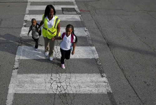 Safe Passage worker Irene Fonder helps two Sherwood Elementary School children cross an intersection in the Englewood neighborhood in Chicago, Illinois, United States, September 8, 2015. The fourth-largest U.S. public school system is not cutting corners when it comes to the $17.8 million annual budget for safety patrols that watch over children walking to school through neighborhoods plagued by gang violence. The school district has expanded the two-year-old Safe Passage program to seven additional schools this year, bringing it to a total of 140 of Chicago's 660 public schools.   REUTERS/Jim Young   - GF10000197899