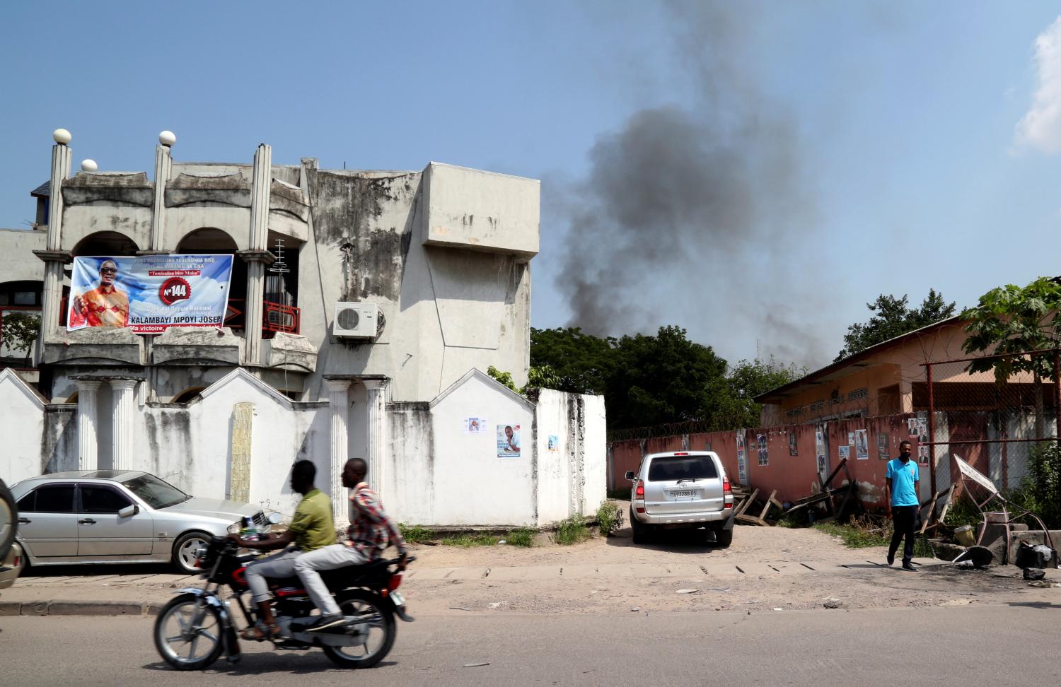 A motorcyclist rides near smoke billowing from fire at the independent national electoral commission's (CENI) warehouse in Kinshasa, Democratic Republic of Congo December 13, 2018. REUTERS/Olivia Acland - RC1D8543AAD0