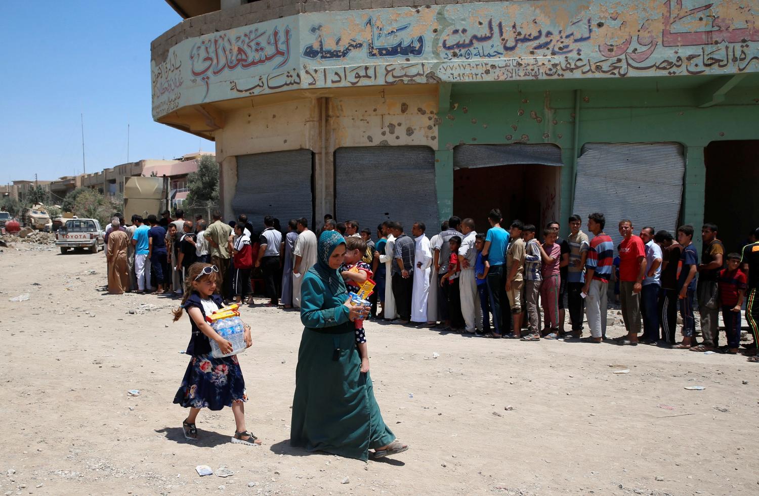 REFILE - CORRECTING PUNCTUATION  Displaced Iraqi residents carry biscuits and bottles of water as they walk past other residents waiting for the food distribution of an aid organization during the first day of Eid al-Fitr celebration in West Mosul, Iraq June 25, 2017. REUTERS/Erik De Castro     TPX IMAGES OF THE DAY - RC19775F43A0