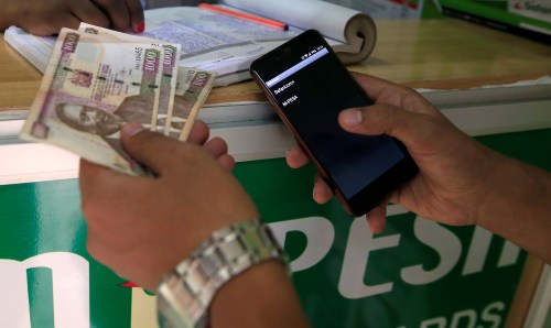 A customer conducts a mobile money transfer, known as M-Pesa, at a Safaricom agent stall, as he holds Kenyan shillings (KSh) in Nairobi, Kenya October 16, 2018. REUTERS/Thomas Mukoya - RC1C78EE9D90