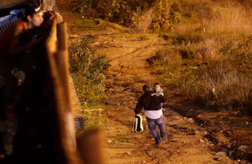 A migrant from Honduras, part of a caravan of thousands from Central America trying to reach the United States, runs with his son after crossing illegally from Mexico to the U.S. by jumping a border fence, as they are photographed through the border wall in Tijuana, Mexico, January 13, 2019.   REUTERS/Mohammed Salem - RC11E5CFADE0