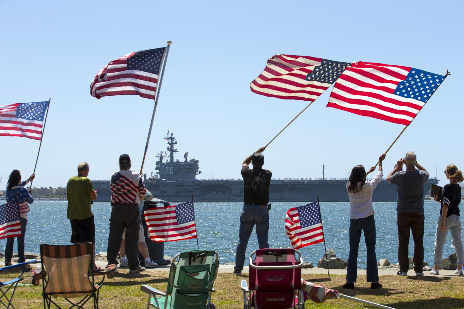 Supporters wave American flags along the shoreline as the USS Ronald Reagan, a Nimitz-class nuclear-powered super carrier, departs for Yokosuka, Japan from Naval Station North Island in San Diego, California  August 31, 2015. The Reagan is replacing the USS George Washington as part of a complicated three-carrier swap that exchanges crews for ships, saving the Navy millions in moving costs.  REUTERS/Mike Blake - GF10000188448