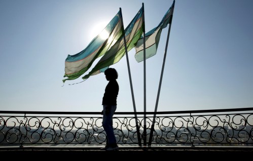 A girl is silhouetted against the sun standing next to Uzbek flags in Tashkent November 5, 2005.    REUTERS/Shamil Zhumatov/File Photo - S1BEUGTDXIAA
