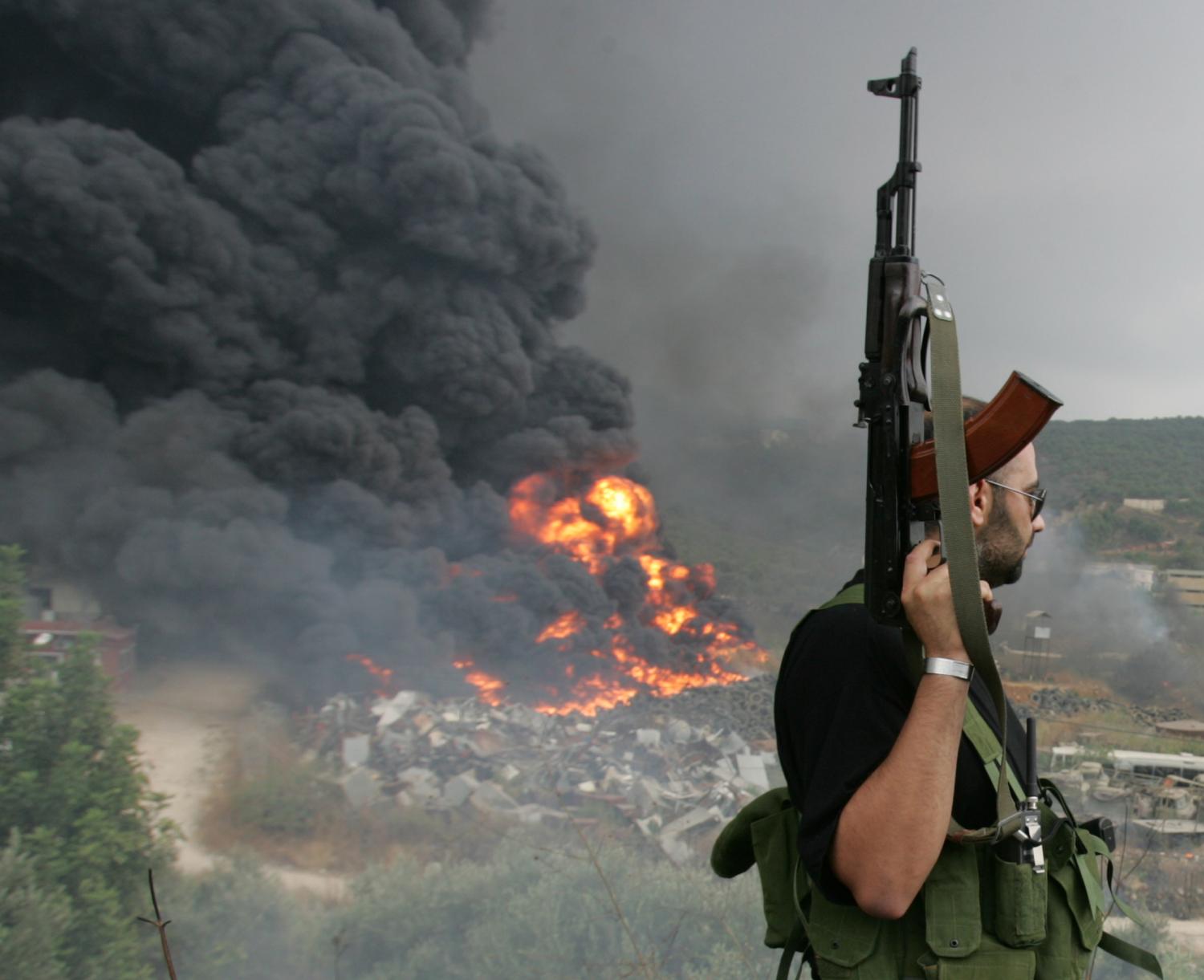 A Lebanese Hizbollah guerrilla looks at a fire rising from a burning object in a Beirut suburb July 17,2006. Israeli Defence Minister Amir Peretz said on Monday that no Israeli jet or helicopter had been shot down over Lebanon but did not rule out that a drone many have been downed.      REUTERS/Issam Kobeisi    (LEBANON) - GM1DTBLBLOAA