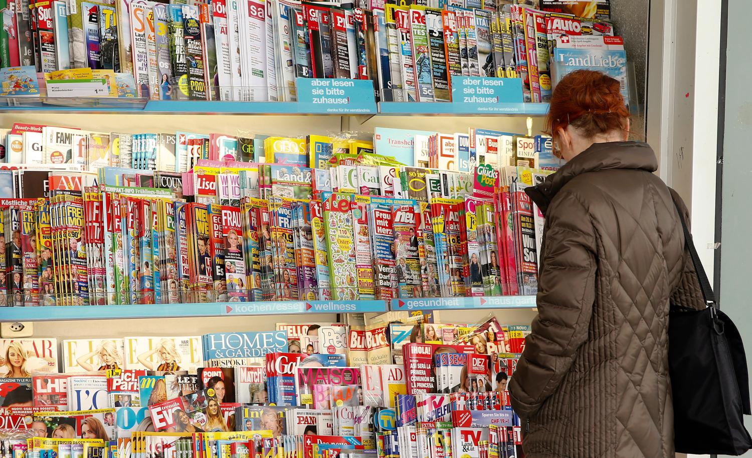 A woman looks at magazines displayed at a kiosk in Zurich March 16 , 2015. One of Switzerland's two big supermarkets, Coop, is to stop selling titles such as German magazine Der Spiegel, the German-language edition of Vogue and a Mickey Mouse comic because it says local distributors have not cut prices after a currency surge. The Swiss central bank's decision on Jan. 15 to end a cap on the value of the currency at 1.20 Swiss francs per euro sent the franc skyrocketing and led to fears for Switzerland's export-reliant economy. REUTERS/Arnd Wiegmann (SWITZERLAND - Tags: MEDIA BUSINESS) - GM1EB3H00BN01