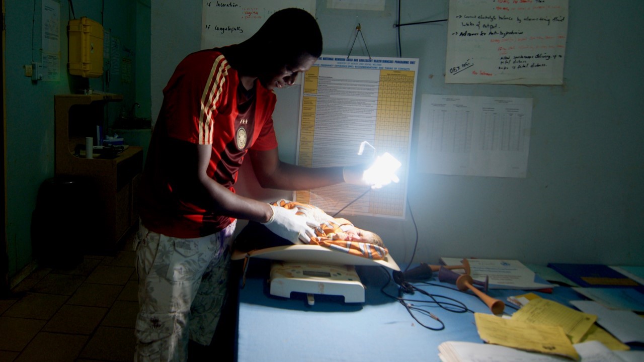 Community Health Worker in The Gambia using We Care Solar suitcase to examine a newly delivered baby