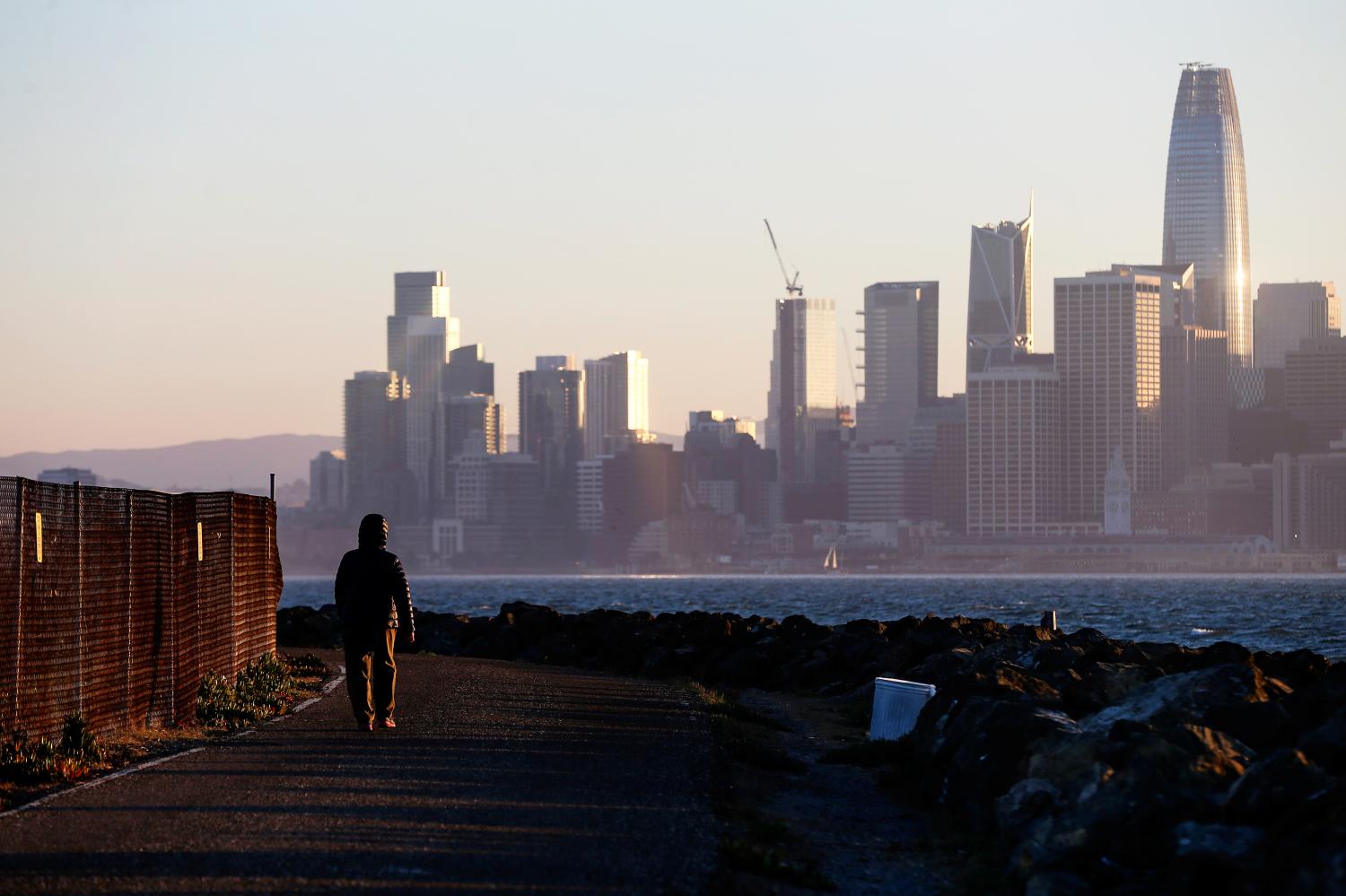 The San Francisco skyline is seen behind a woman as she walks past a condemned area on Treasure Island, near San Francisco, California, U.S. October 18, 2018.  Picture taken October 18, 2018.     To match Special Report USA-MILITARY/LEGACY  REUTERS/Elijah Nouvelage. - RC1EDF07AC90