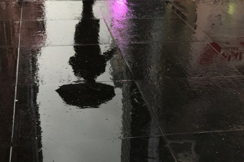 A man is reflected in a puddle as he walks with an umbrella in Times Square in the Manhattan borough of New York City, New York, U.S., February 7, 2018. REUTERS/Carlo Allegri - RC18541FABC0