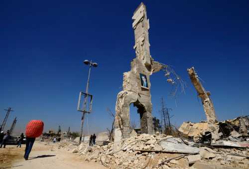 A picture of Syria's President Bashar al-Assad is displayed on a damaged structure at the entrance of al-Dukhaneya neighbourhood near Damascus, as civilians carry their belongings recovered from their homes after soldiers loyal to Syria's President Bashar al-Assad regained control of the area from rebel fighters October 7, 2014. REUTERS/Omar Sanadiki   (SYRIA - Tags: POLITICS CIVIL UNREST CONFLICT TPX IMAGES OF THE DAY) - GM1EAA71PL001