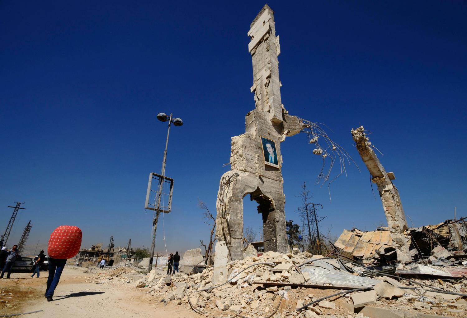 A picture of Syria's President Bashar al-Assad is displayed on a damaged structure at the entrance of al-Dukhaneya neighbourhood near Damascus, as civilians carry their belongings recovered from their homes after soldiers loyal to Syria's President Bashar al-Assad regained control of the area from rebel fighters October 7, 2014. REUTERS/Omar Sanadiki   (SYRIA - Tags: POLITICS CIVIL UNREST CONFLICT TPX IMAGES OF THE DAY) - GM1EAA71PL001