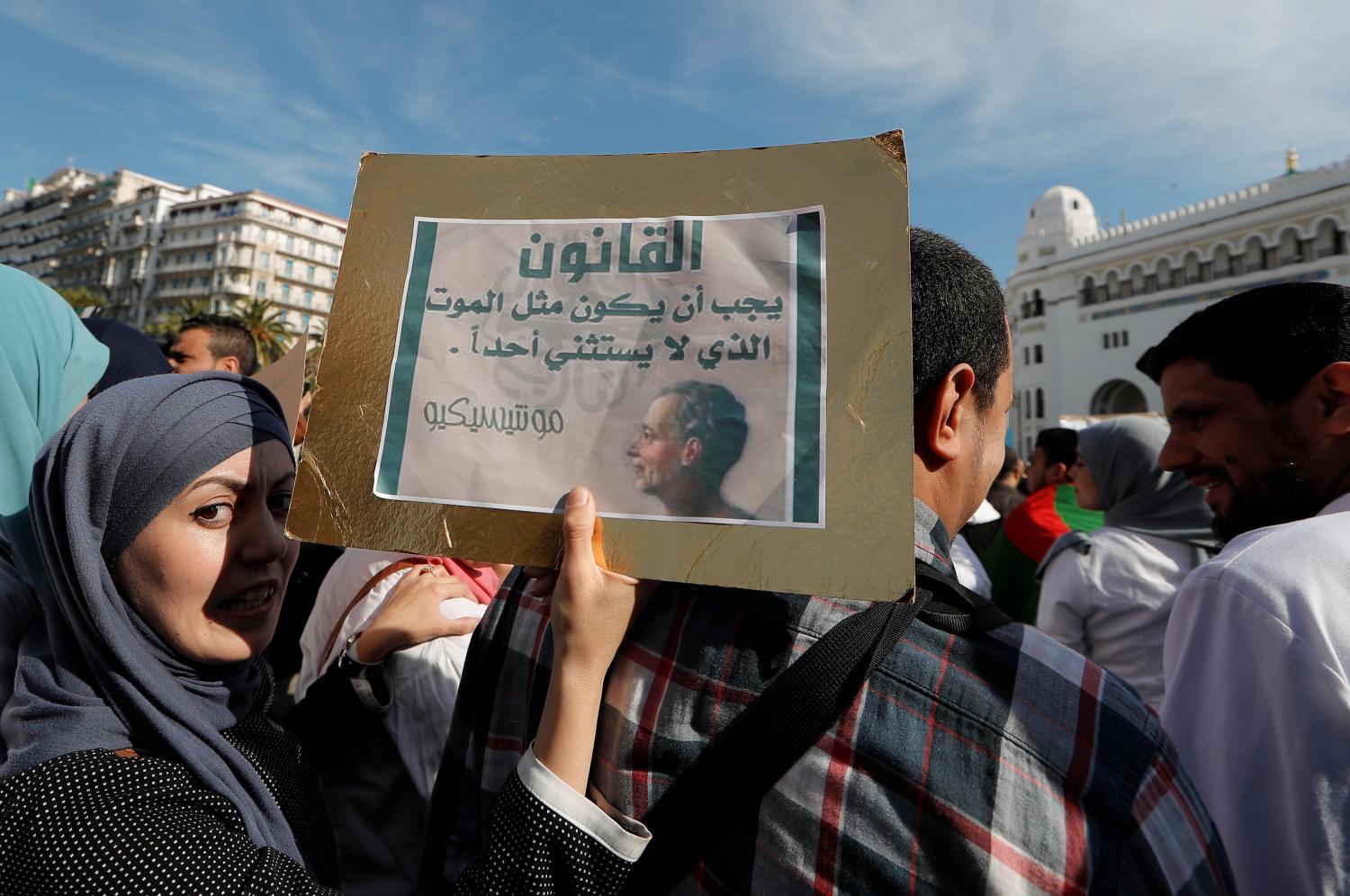 A demonstrator carries a sign as teachers and students take part in a protest demanding immediate political change in Algiers, Algeria March 13, 2019. The sign reads: "The law should be like death, which spares no one". REUTERS/Zohra Bensemra - RC1D6736BA50
