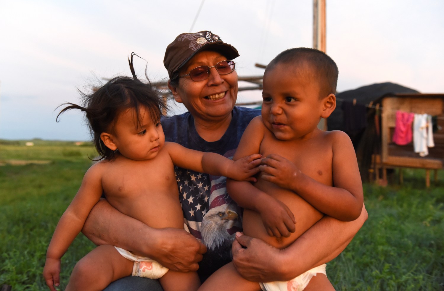 Beatrice Lookinghorse sits with two of her grandchildren, Linda Lookinghorse and Cody James Lookinghorse, in the backyard of her home on the Cheyenne River Reservation in Green Grass, South Dakota, U.S., May 28, 2018. Beatrice Lookinghorse is related to several of the Fort Laramie treaty riders who live with her. Beatrice also raises other children from the extended Lookinghorse family. "I promised my father that none of his grandkids would ever be put in the (foster care) system," she said. REUTERS/Stephanie Keith  SEARCH "KEITH ANNIVERSARY" FOR THIS STORY. SEARCH "WIDER IMAGE" FOR ALL STORIES. - RC1A57AAB7F0