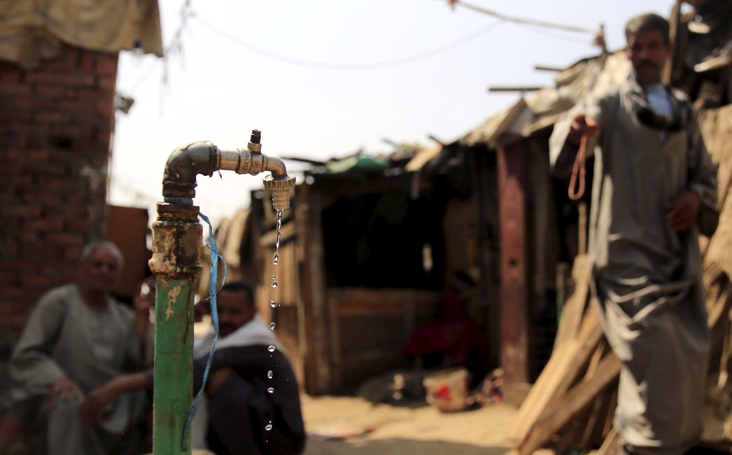 Water drips from a tap as people sit in the Eshash el-Sudan slum in the Dokki neighbourhood of Giza, south of Cairo, Egypt September 2, 2015. Residents of the slum clashed with police in late August, when about 50 ramshackle huts were destroyed and at least 20 people were injured by teargas, local media reported, as authorities attempt to clear the area and rehouse residents. The slum dwellers, some of whom have called Eshash el-Sudan home for 50 years, say there are not enough apartments built nearby to house them. The residents of the slum eke out a living by disposing of rubbish or baking bread. Schooling is too expensive for most of their children, who play with salvaged rubbish amid shacks made out of discarded wood and leather. REUTERS/Amr Abdallah DalshSEARCH "ESHASH EL-SUDAN" FOR ALL PICTURES  - GF10000200359