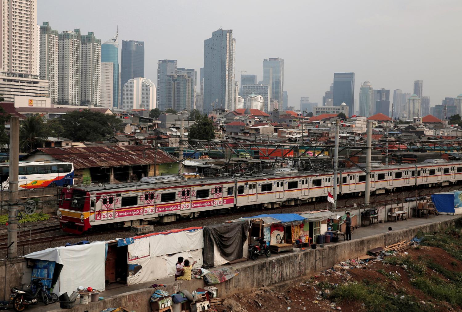 People sit in front of makeshift living quarters, as a commuter train passes through, near a slum area in Jakarta, Indonesia September 12, 2017. REUTERS/Beawiharta - RC1D83C7C230