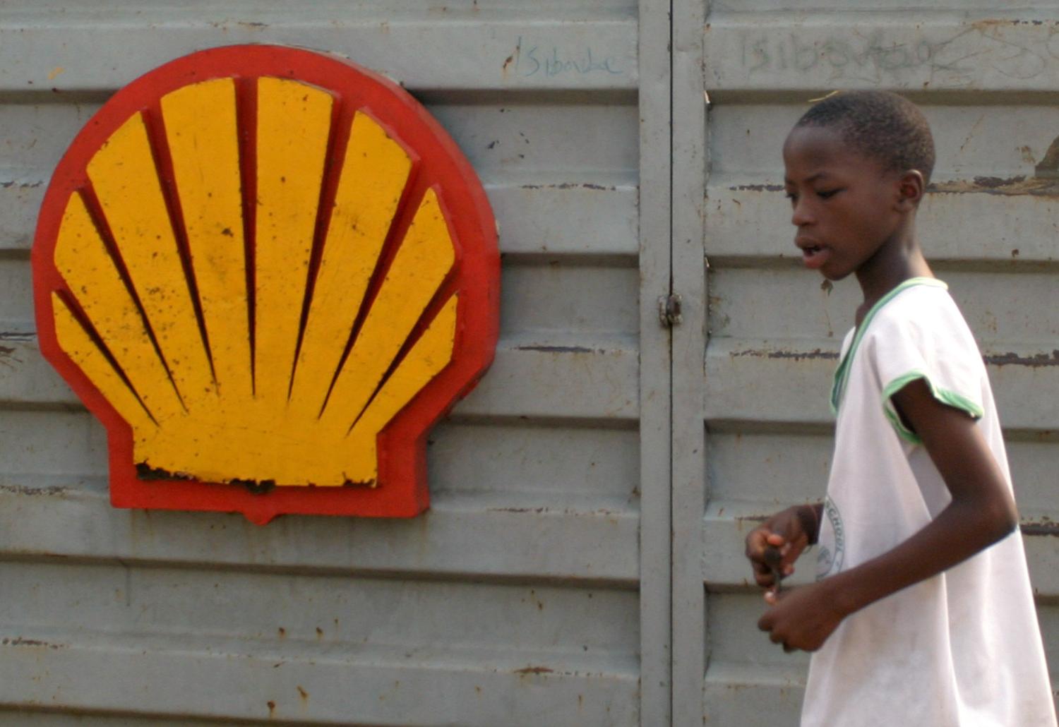 A Nigerian schoolboy walks past the logo of Dutch oil giant Shell near Warri in the volatile Niger-Delta region January 17,2006. World oil prices hit a three and half-month high on Tuesday after militants said they would broaden attacks on Nigeria's oil industry, threatening to cut deeper into supplies from the world's eighth biggest exporter. REUTERS/George Esiri - RP3DSFDKUHAD