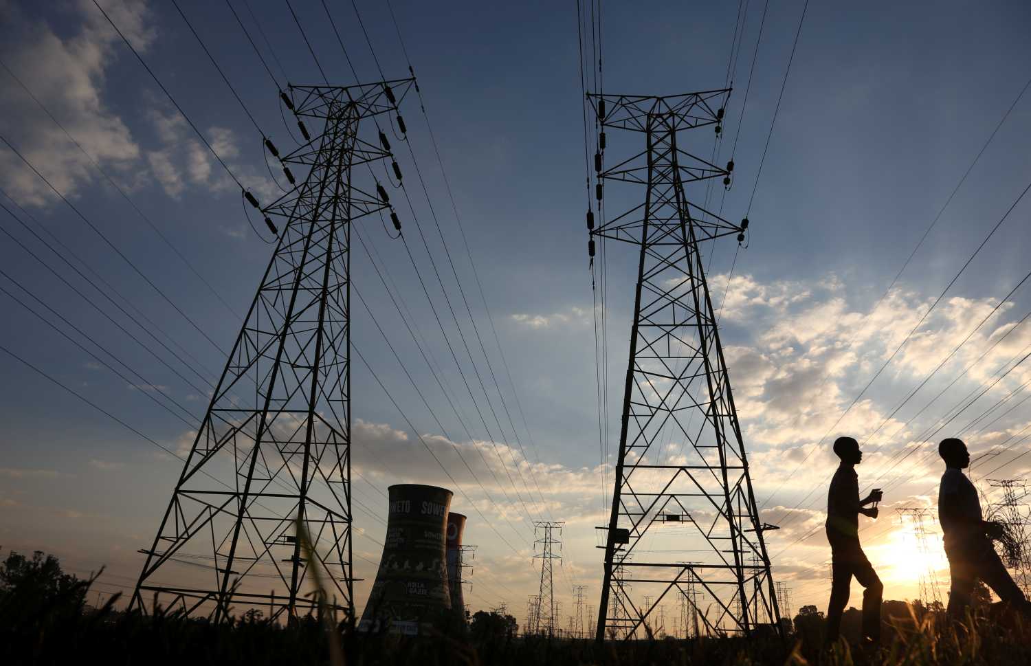 Boys walk past electricity pylons and the cooling towers of the defunct Orlando Power Station in Soweto, South Africa, June 28, 2018. Picture taken June 28, 2018. REUTERS/Siphiwe Sibeko - RC164C8E8250
