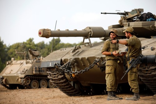 Israeli soldiers speak next to a tank as military armoured vehicles gather in an open area near Israel's border with the Gaza Strip October 18, 2018. REUTERS/Amir Cohen - RC11CEB9C060