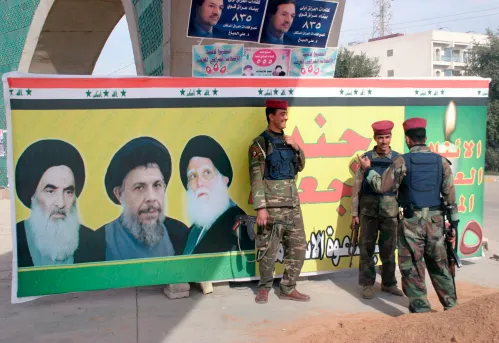 Iraqi soldiers stand guard near an election poster featuring pictures of Shi'ite leader Grand Ayatollah Ali Sistani (L), and slain clerics Ayatollah Mohammad Baqir al-Hakim (C) and Ayatollah Mohammad Sadeq al-Sadr in the holy city of Najaf December 6, 2005. Iraqis will go to the polls December 15 to elect their first full, four-year parliament since the fall of Saddam Hussein. REUTERS/Ali Abu Shish - RP2DSFIILWAB