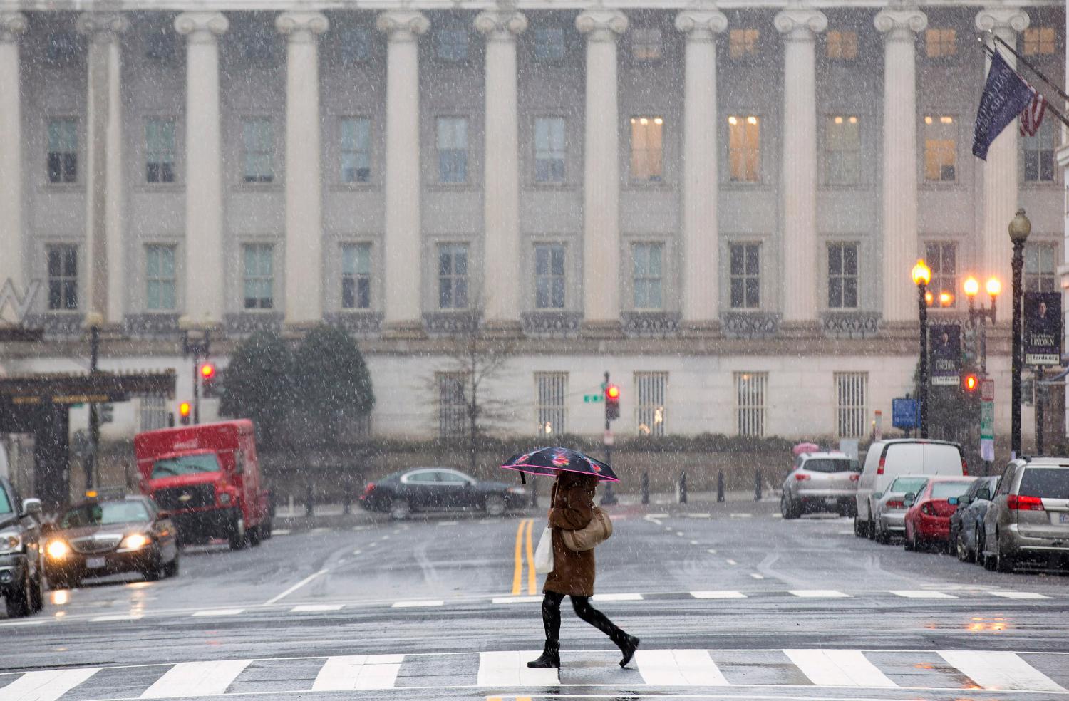A woman crosses a nearly empty street at rush hour, near the U.S. Treasury Building during a snow storm in Washington March 5, 2015. A large winter storm reaching from Texas to southern New England, which prompted school closings and led to almost 2,300 flight cancellations, had dumped over a foot (30 cm) of snow on parts of the eastern United States by early Thursday morning. REUTERS/Joshua Roberts (UNITED STATES - Tags: ENVIRONMENT SOCIETY) - GM1EB351UKX01